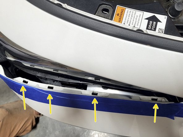 INTEGRA: Use a forceful but controlled motion with both hands to pop the bumper out of the four headlight clips as shown