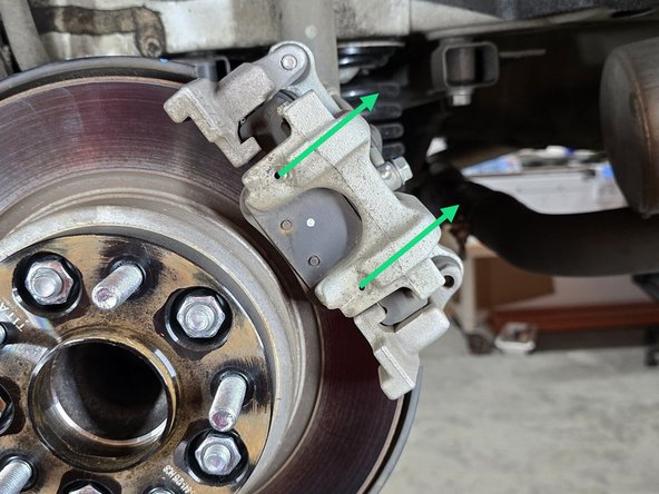 Using a 7mm Allen head socket and a 3/8" drive ratchet, remove the two caliper slider bolts circled in yellow