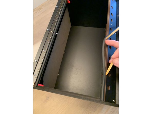 Continue to trim the provided gasket material and affix to the exit panel at the base of the box as shown. Be sure to move the lid prop out of the way to get the gasket going all the way flush with the sidepanel.