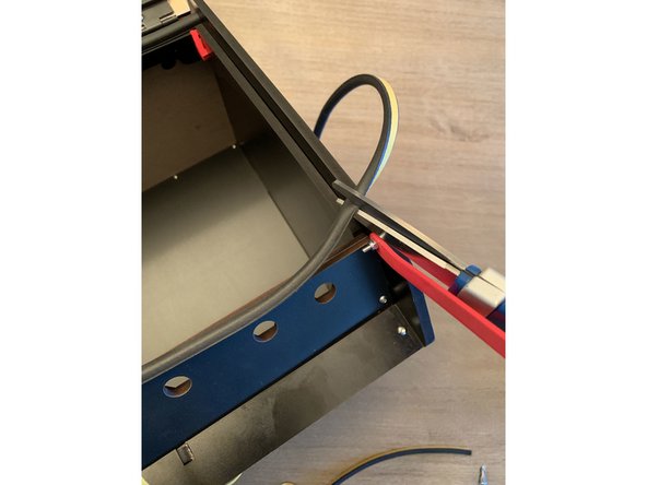Continue to trim the provided gasket material and affix to the exit panel at the base of the box as shown. Be sure to move the lid prop out of the way to get the gasket going all the way flush with the sidepanel.
