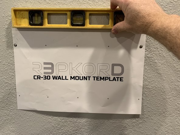 Press a tack through the top right hole of the template, ideally over the stud you marked and then using a level tack up the other side once you've verified that the top of your template is indeed level.
