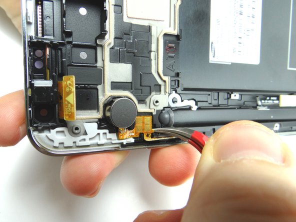 Wedge the Curved Tip Tweezers in the closed position under the contact pad connected to the vibrator and pry up to loosen it.