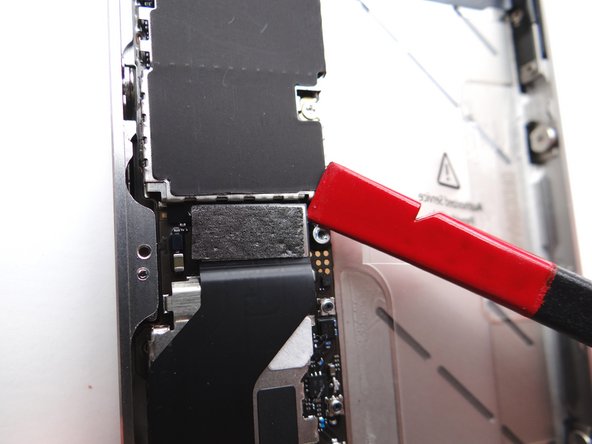 Picture 1: Place flat end of spudger under upper-right corner of the charging port assembly cable. Gently twist your hand clockwise releasing the cable from its socket on the logic board.