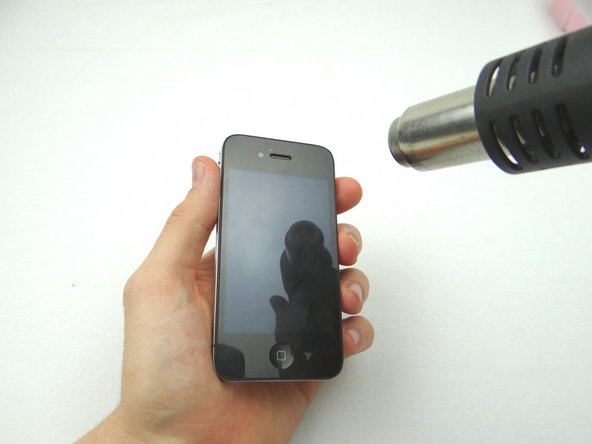 Picture 1: Apply low heat (100 degrees celsius) to the top and bottom edges of the iPhone, sweeping back and forth to loosen adhesive.  Continue for two minutes.