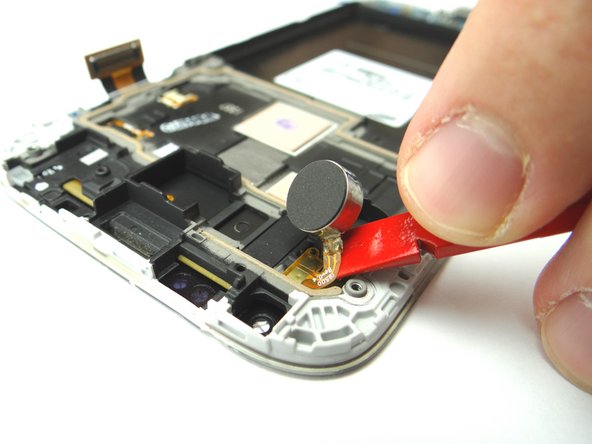 Once the vibrator is free from the adhesive, use the Black Spudger to gently pry up the vibrator ribbon contacts. Place the vibrator in COMPARTMENT G.