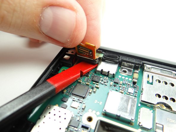 Peel assembly away from rear case with your fingers.  Slide flat end of spudger under assembly to push through the mild adhesive holding it down.