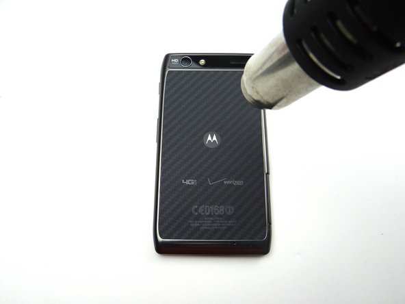 Picture 1: Apply low-level heat (100° Celcius) all over the back of the phone for 60 seconds to loosen the adhesive securing the battery cover.  Apply heat to the Motorola symbol in the middle for an additional 15 seconds.