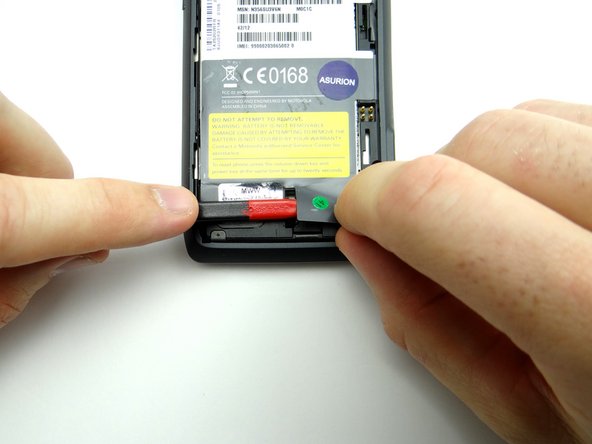 Use the flat edge of the spudger to lift the tab on the lower-right corner of the IMEI sticker.  Grab the tab with your fingers and hold it back.