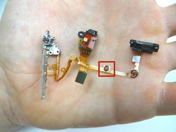 Seat the contact (red square in Picture 1) on the notch on the rear case first (red square in Picture 2).  Then line up and adhere the cable on either side of the notch.