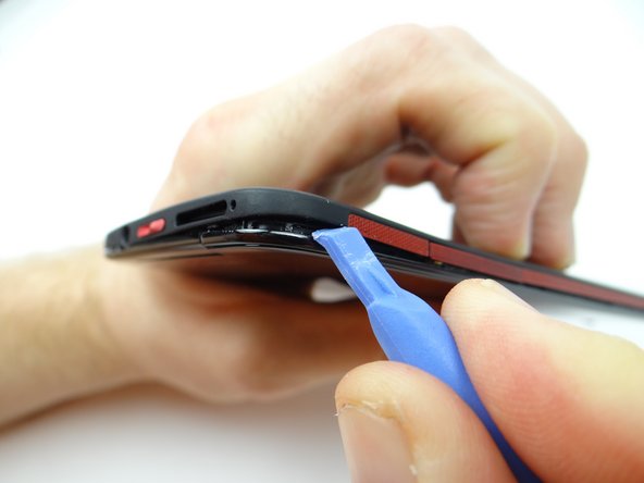 Push the upper-right corner up with a guitar pick, then insert a blue pry tool to continue working up the corner.