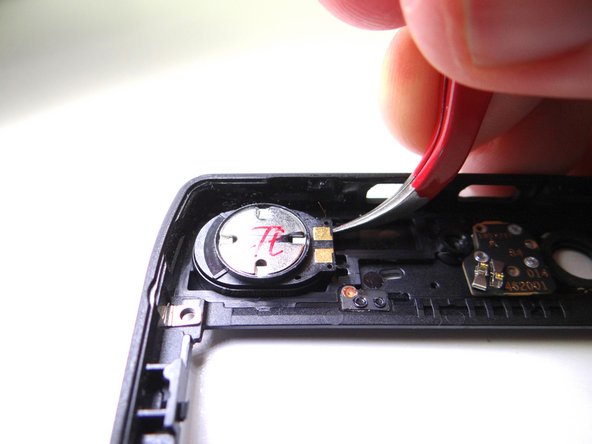 Picture 2: Wedge the curved-tip tweezers in the closed position under the speaker.  Pry up to free it.