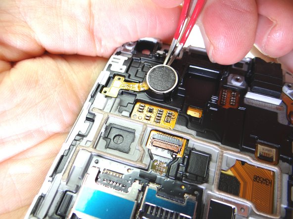 Picture 1: With the curved-tip tweezers in the closed position, wedge the tip under the vibrator and pry up enough to grab the vibrator with your fingers.