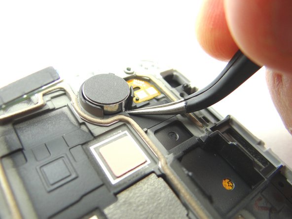 Picture 1: Wedge the Curved Tip Tweezers in the closed position under the vibrator. Pry up to free the vibrator from the adhesive holding it to the front panel assembly.