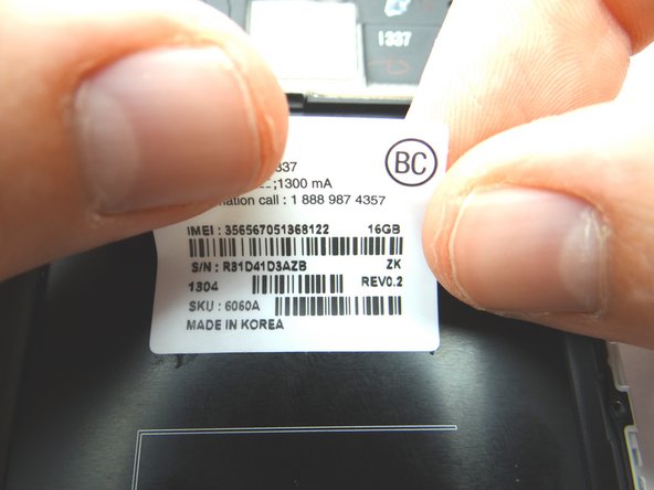Use your finger nail or tweezers to lift the corner of the sticker and peel up.  Move it immediately to the replacement part.