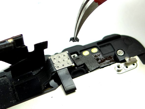 Loosen your grip on the tweezers just enough to put tension on the spacer.  Lift the spacer away from the phone and drop it in your hand.