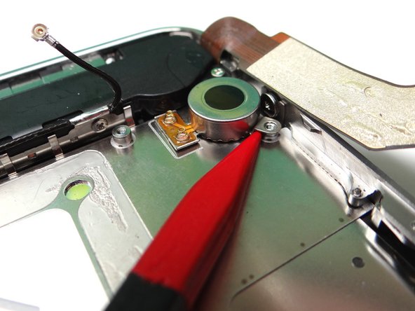 Picture 1: Wedge the pointed tip of the Black Spudger under the lip of the vibrator.  Gently lift to loosen the adhesive holding the vibrator to the mid-frame.