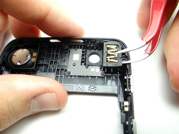 Picture 1: Wedge a single prong of the curved-tip tweezers under the adhesive frame covering the headphone jack.