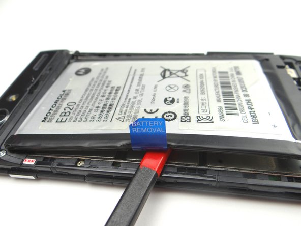 Picture 2: Wedge spudger underneath battery.  Pry up around the edges to free the adhesive holding down the battery.