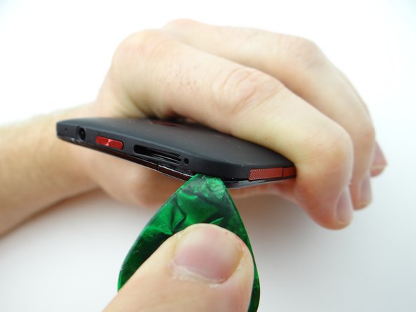 Push the upper-right corner up with a guitar pick, then insert a blue pry tool to continue working up the corner.