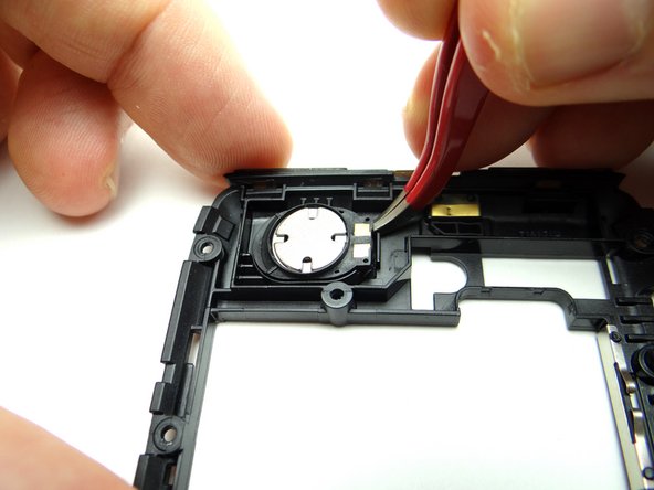 Wedge the curved-tip tweezers in the closed position under the corner of the speaker as shown.  Gently pry up the corner just enough to grab it with your fingers.