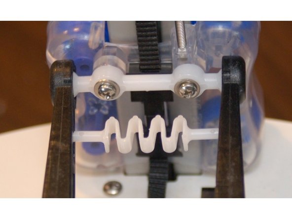 Gently stretch the spring across to the opposite arm and latch it into the keyhole notch.