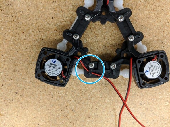 Looking down at the effector platform, route the left fan's wires through the clip at the end of the mounting bracket as indicated by the blue circle.