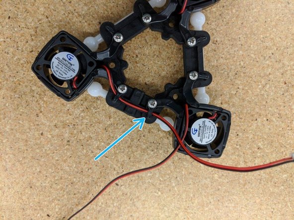 Finish routing the left fan's wire by running it under the clip next to it (blue arrow) and then fold the lead under the effector (red circle).