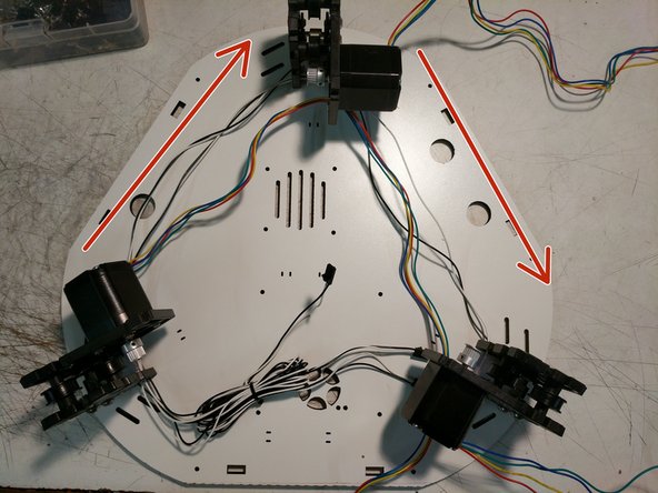 You will now route the stepper motor wires in the opposite direction that you routed the end stop wires. Note the arrows on the image for direction. The wires will route through the motor mount plate in the location indicated by a red arrow in the first image.