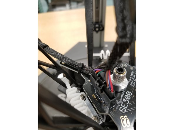 Rout the power and thermistor section of the whip to the back left of the hotend and zip tie around the mesh loom and the hotend board arm as shown.