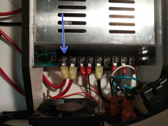 The 700mm long 12awg red wire that you previously crimped the ring terminal on should now be connected to the power supply in the location indicated by an arrow. Route the wire under the PSU blocker with other red 12awg wire.