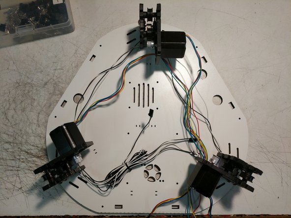 You will now route the stepper motor wires in the opposite direction that you routed the end stop wires. Note the arrows on the image for direction. The wires will route through the motor mount plate in the location indicated by a red arrow in the first image.