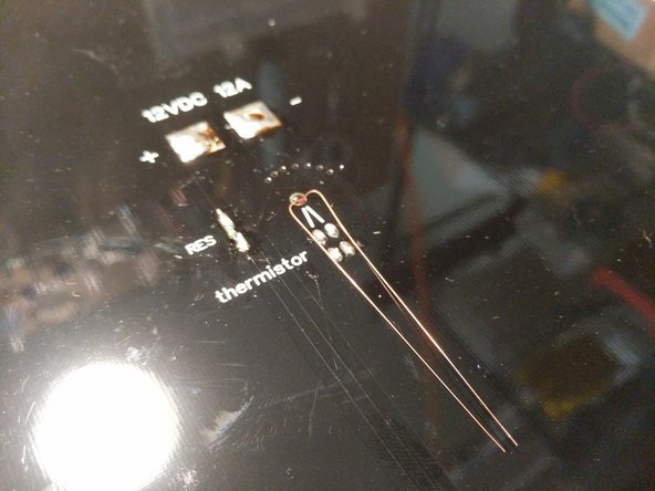 Separate the legs of the thermistor as shown and insert the glass bead of the thermistor into the hole in the center of the heated bed. Solder them to the top two pads on the heated bed.