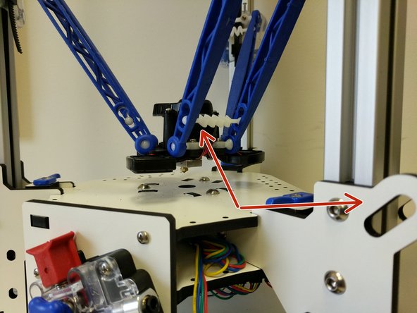 Identify the Z Tower. Insert a tension spring between the two arms at the end where the hotend will be installed.  Install that set of arms on the hot end in line with the fan that is vertical (indicated with red arrows)