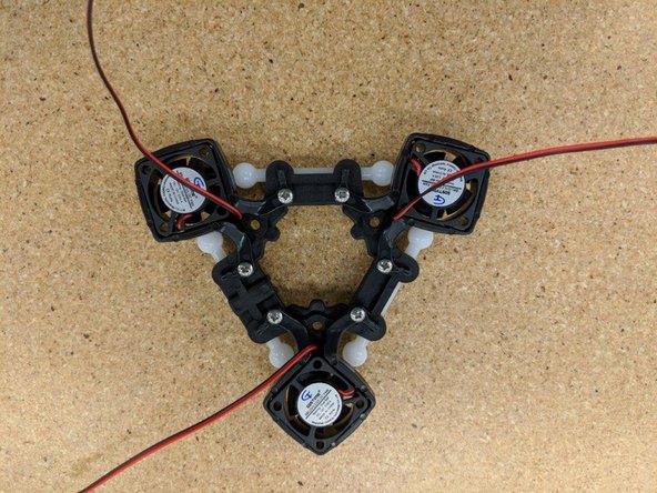 Looking down at the effector platform, route the left fan's wires through the clip at the end of the mounting bracket as indicated by the blue circle.