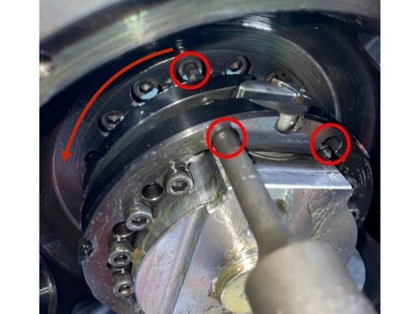 There are 21 mounting screws in the turret that need to be loosened in order to align the turret in the Y Axis. They are located behind the gearhead. There is an area where there are no mounting screws, it is marked on the photo with a curved arrow. See Photo 1