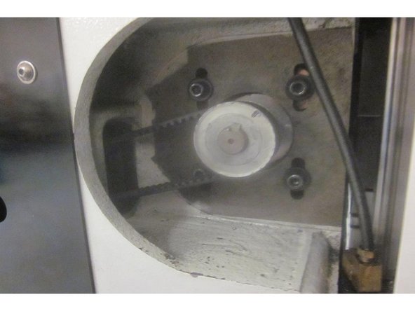 With the servo drive (box attached to the motor) facing the rear of the machine, lift the motor while rotating the servo  box downward into the X axis cavity at the rear of the machine. The servo housing faces down when the motor is installed. Start the 1/4-20 screws.