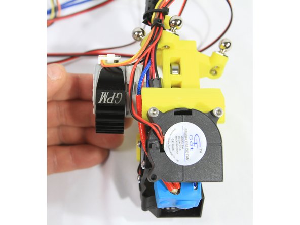 Remove the pink plastic film from the tape and snap the heat sink around the extruder stepper motor oriented down as shown in the second photo.