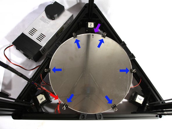 Flip the heated bed over so the aluminum surface faces up as shown in the photo. The wiring harness should exit at the 7 o'clock position as indicated by the red arrow.