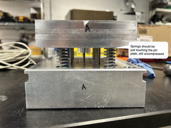 Slide the pin plate assembly into the mud plate. The thick guide pins should line up with the springs and slide into their larger respective holes. Stop once the pin plate is sitting on top of the springs but not compressing them. The plate may end up slightly unlevel, which will be corrected in the next step.