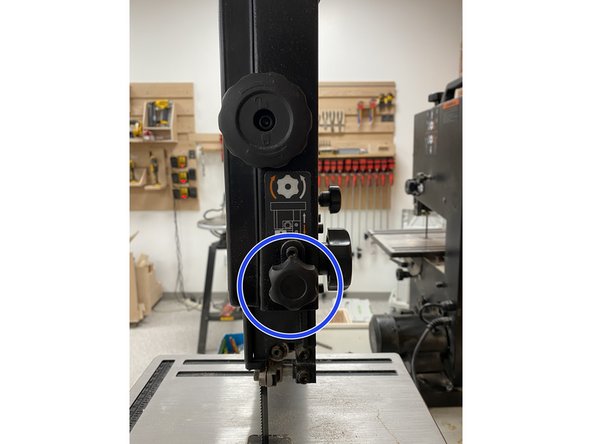 First, loosen the knob on the back of the band saw to unlock the position of the blade guard