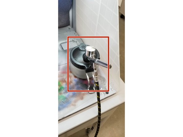 After you finish using a color or paint in the airbrush, fill the paint hopper partway with airbrush cleaner fluid. Spray the cleaner through the brush and into the waste container, making sure to move the control button back and forth as you do to clean the needle. Clean remaining paint from the hopper with IPA, paper towels, and cotton swabs.