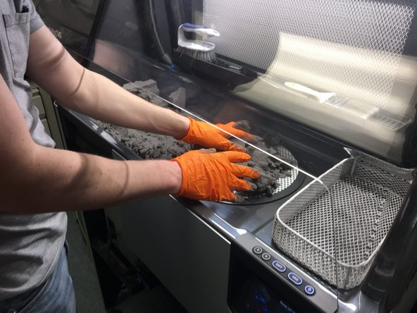 Push the bulk of the powder cake into the grate. As you uncover parts, place them in the wire tray to the right of the work area. We will clean them better in the next steps.