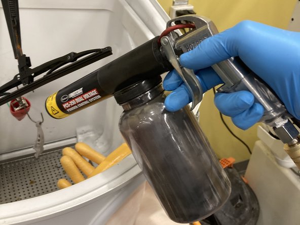 Hold the activator in one hand and the powder gun in the other, with the nozzle pointed down into the tub, towards the part