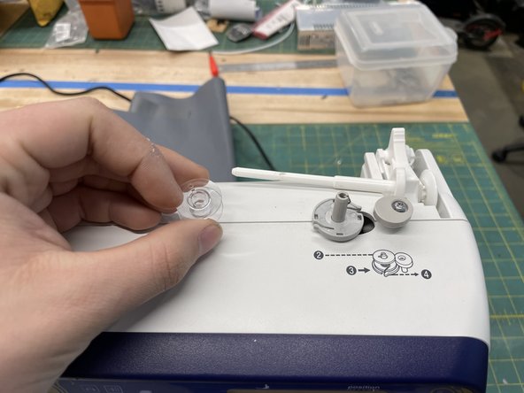 Place the spool on the grey peg on top of the sewing machine. hen push the entire assembly to the right to engage the system.