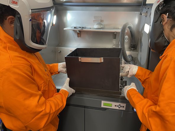With a partner, move the build box from the drying oven to the powder station
