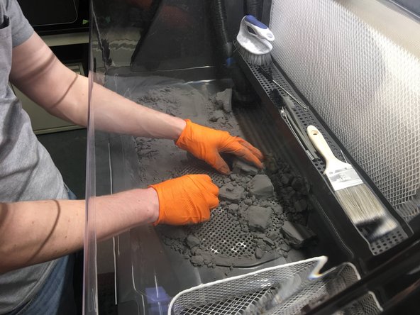 Push the bulk of the powder cake into the grate. As you uncover parts, place them in the wire tray to the right of the work area. We will clean them better in the next steps.