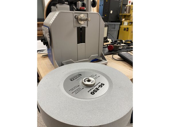 While holding the leather wheel steady, push the grindstone clockwise (against the normal operating motion) and the threaded tension lock should come free. Unscrew the lock and the grindstone will now be free to take off.