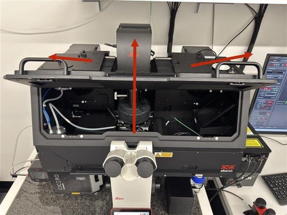 Slide the side panels at the top of the transmitted light arm to the side, then fold the transmitted light arm backwards and open the front flap of the Okolab incubator cage.