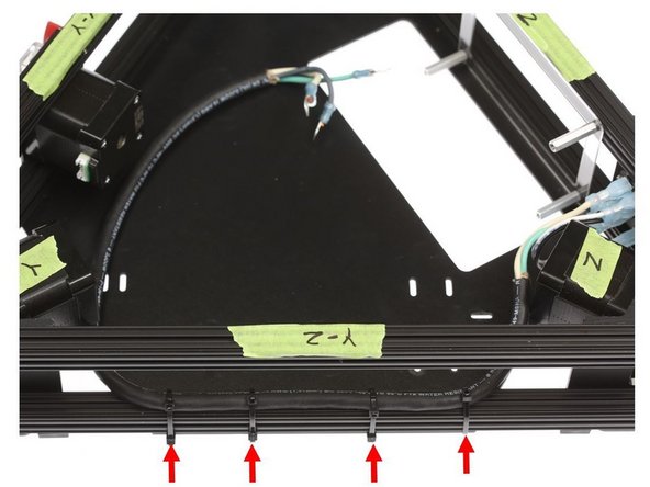Daisy-chaining the included zip ties, secure the AC wiring bundle to the lower Y-Z OpenBeam extrusion on the printer, looping the zip tie through the oval opening on the power supply mount panel.